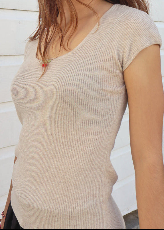 Woman wearing a beige ribbed sweater against a white wooden panel background