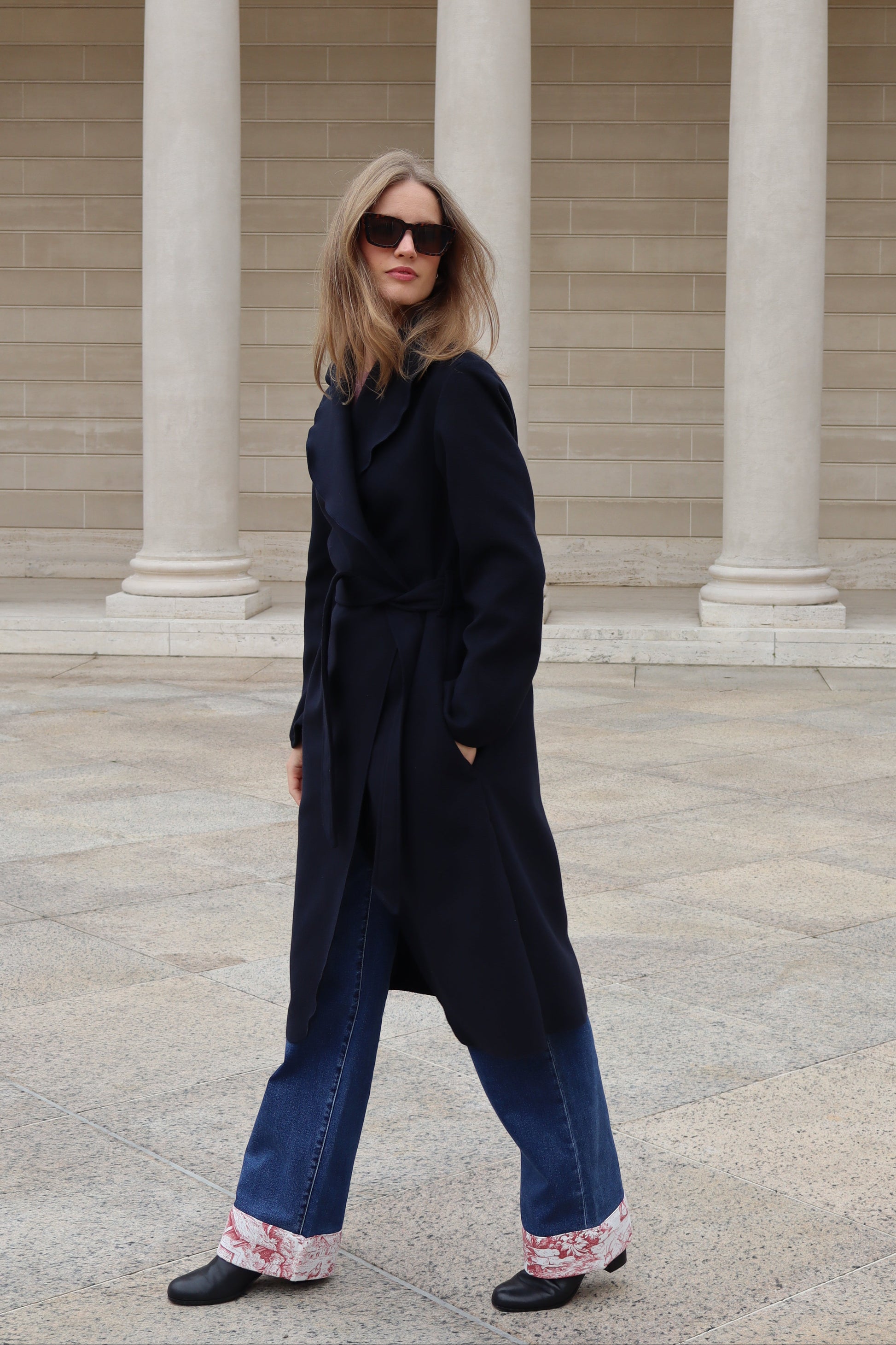 Blonde woman in navy coat and jeans and retro sunglasses
