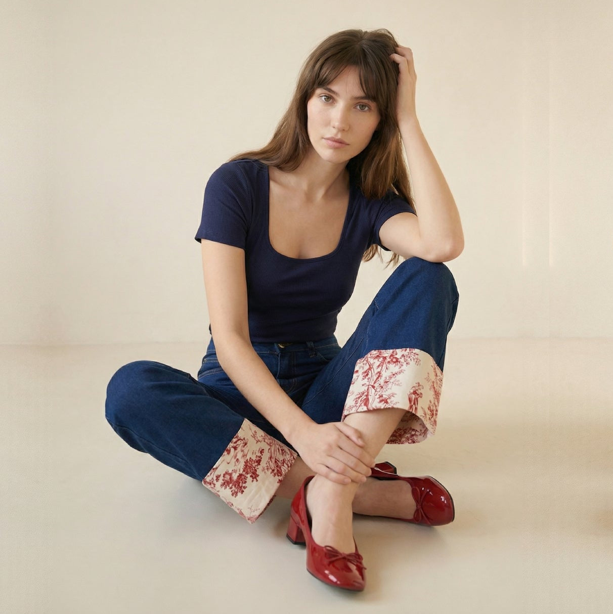 Woman sitting on a light-colored floor wearing a navy outfit with floral cuffs.