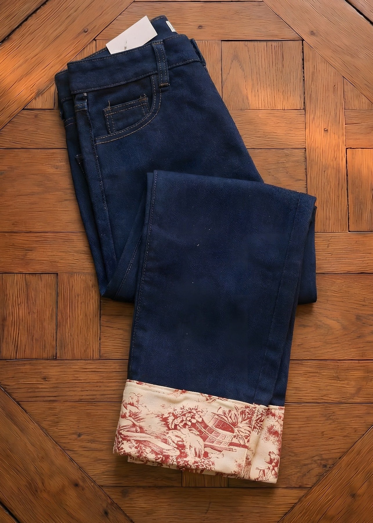 Folded blue jeans with a patterned hem on a wooden floor