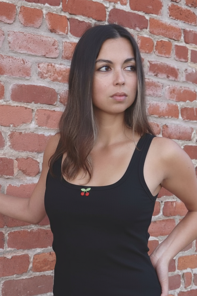 Woman wearing a black tank top with a design against a brick wall