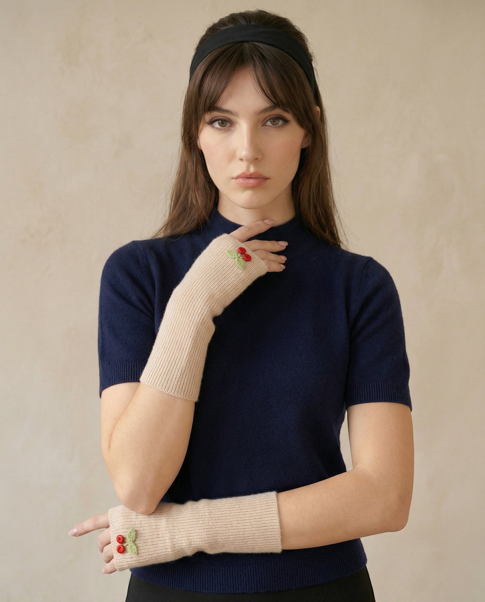 Woman wearing navy blue top and beige fingerless gloves with red details against a neutral background