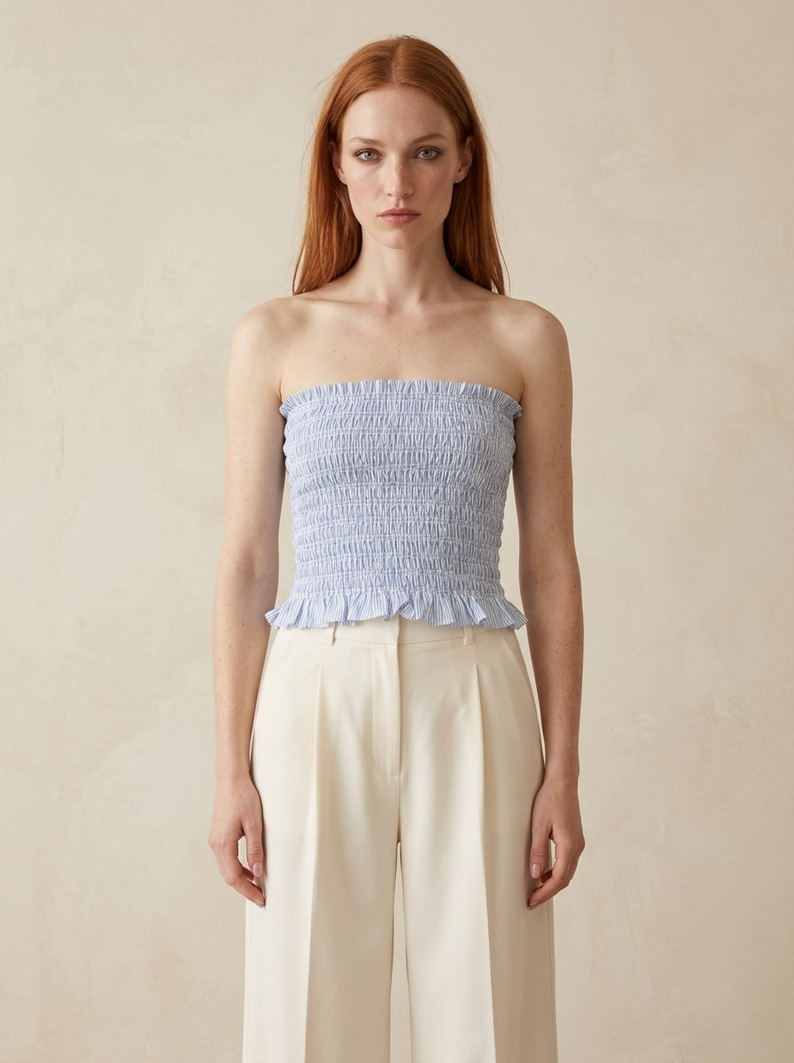 Woman wearing a light blue strapless top and beige pants against a beige background