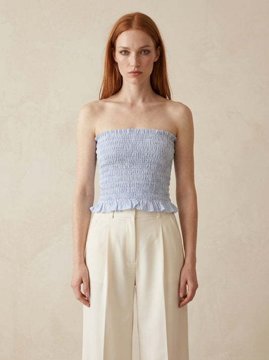 Woman wearing a light blue strapless top and beige pants against a beige background