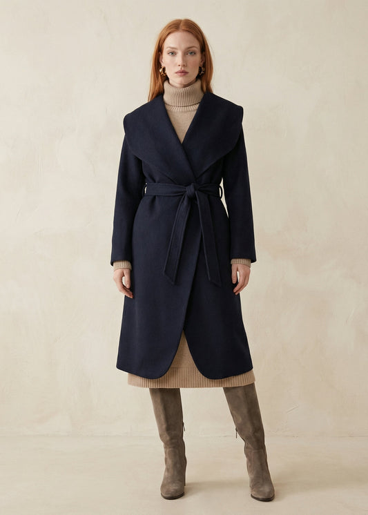 Woman wearing a navy coat with a beige sweater and brown boots on a neutral background