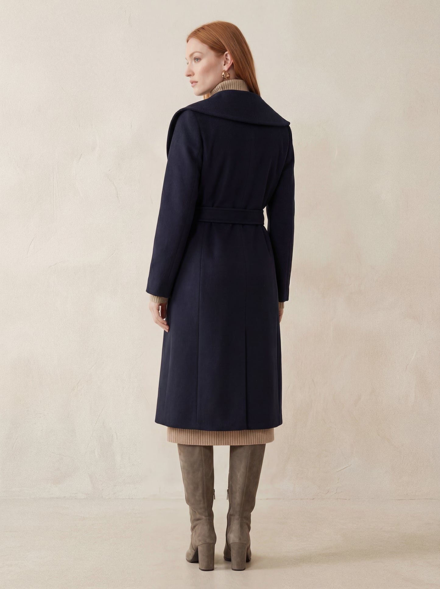 Woman wearing a navy coat standing against a beige background