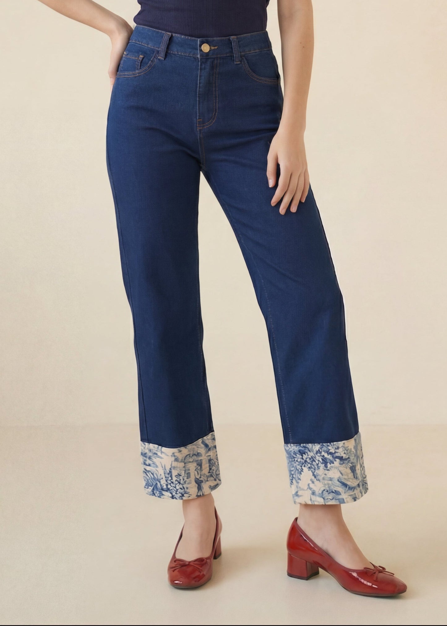 Woman wearing a navy top and blue jeans with floral cuffs on a beige background
