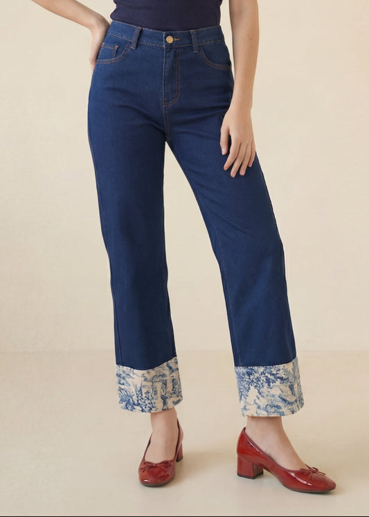 Woman wearing a navy top and blue jeans with floral cuffs on a beige background