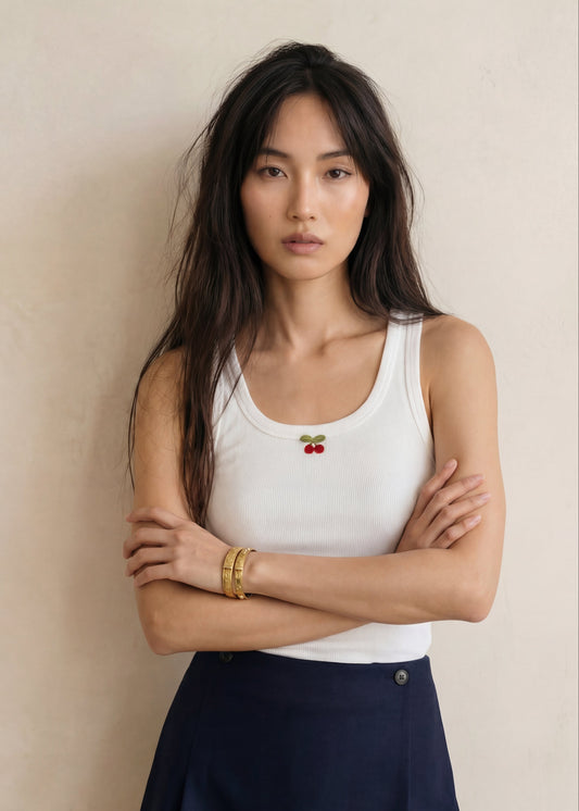 Woman wearing a white tank top with a red logo and a navy blue skirt against a beige background