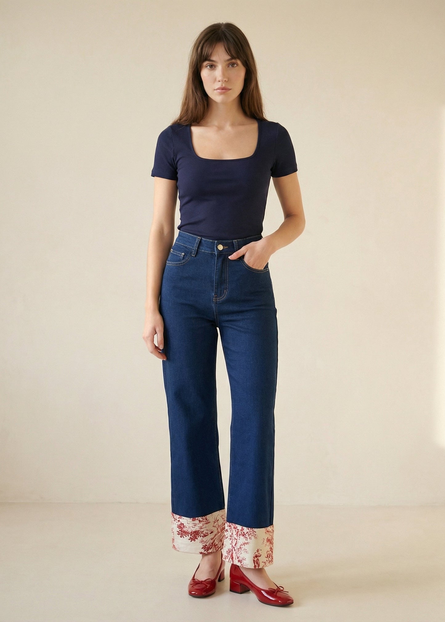 Woman wearing a navy top and blue jeans with floral cuffs on a beige background