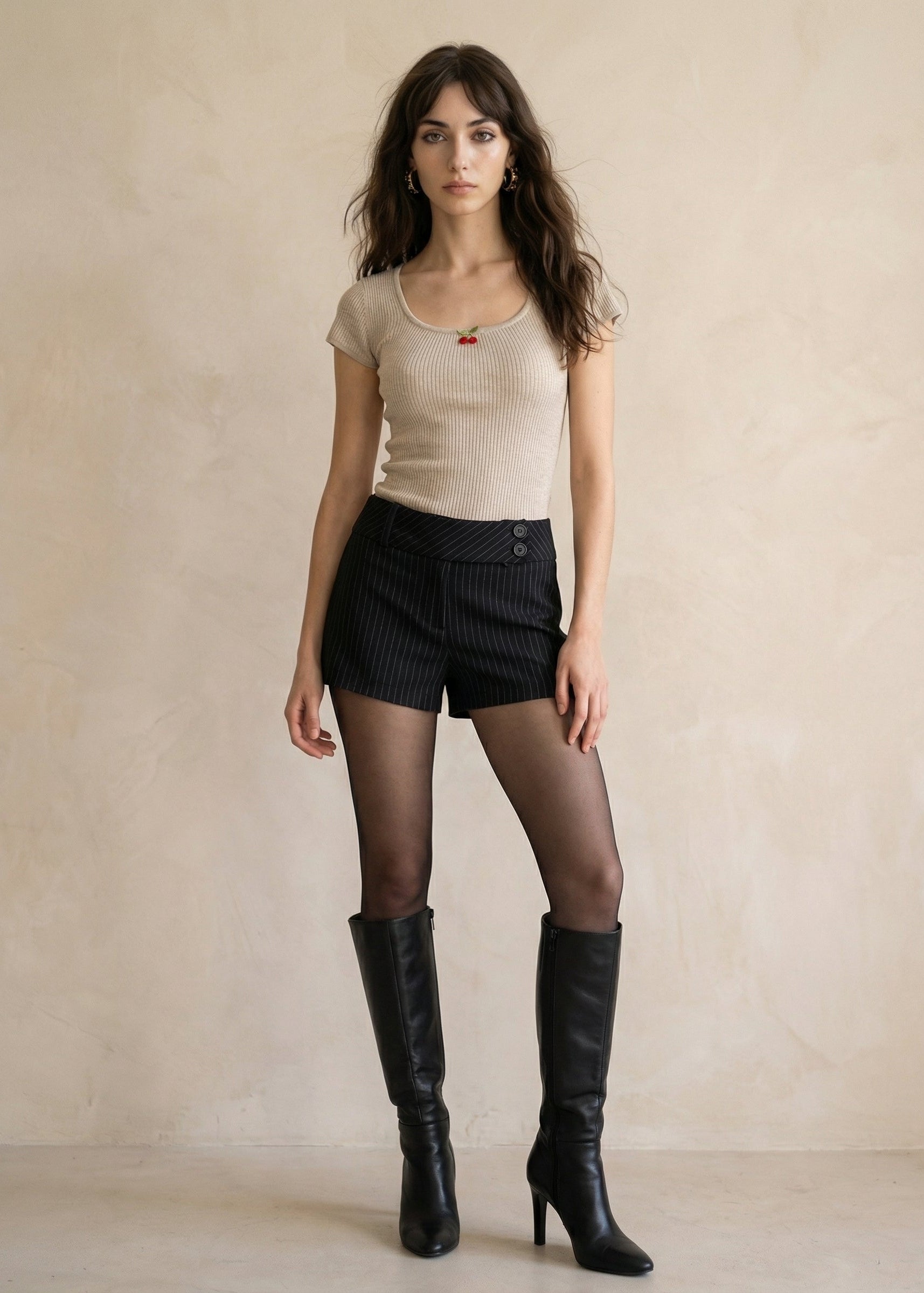 Woman wearing a beige top, black shorts, and black knee-high boots against a plain background