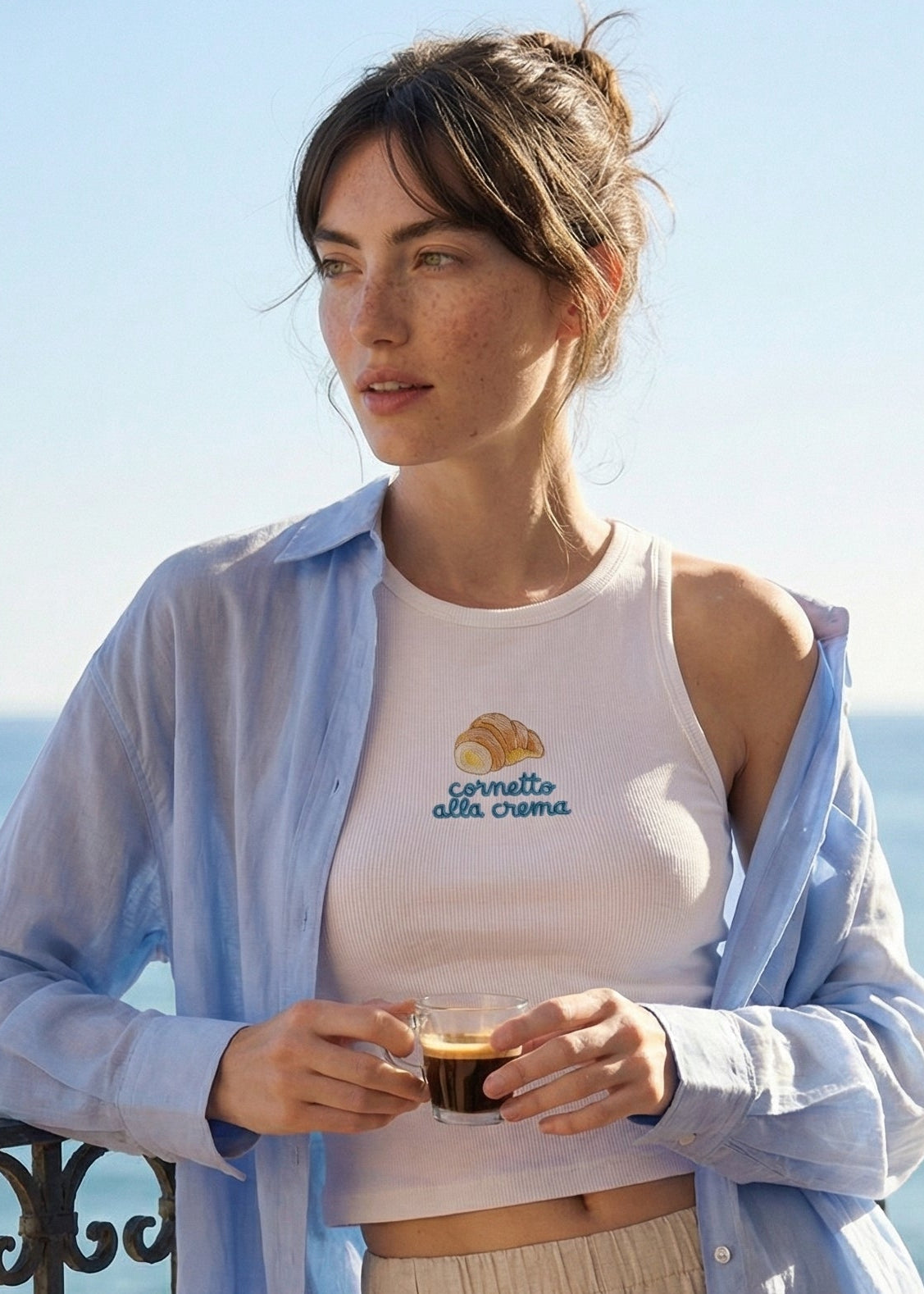 Woman standing on a balcony overlooking the ocean, holding a coffee cup.