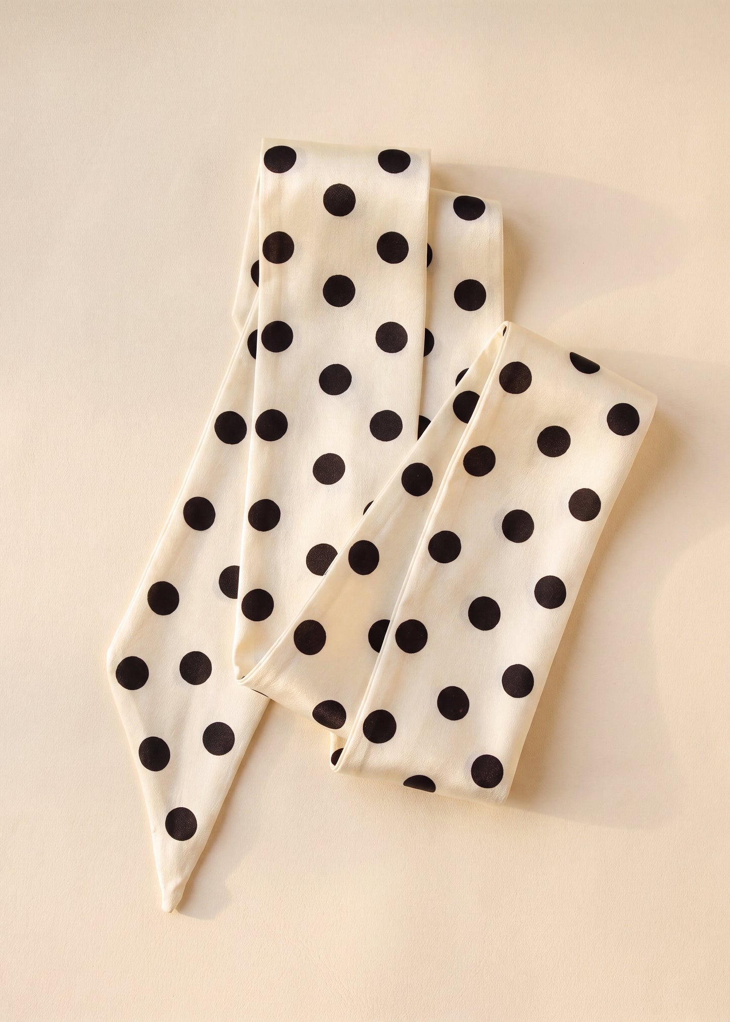 A cream-colored silk scarf with black polka dots, folded neatly on a light beige background.