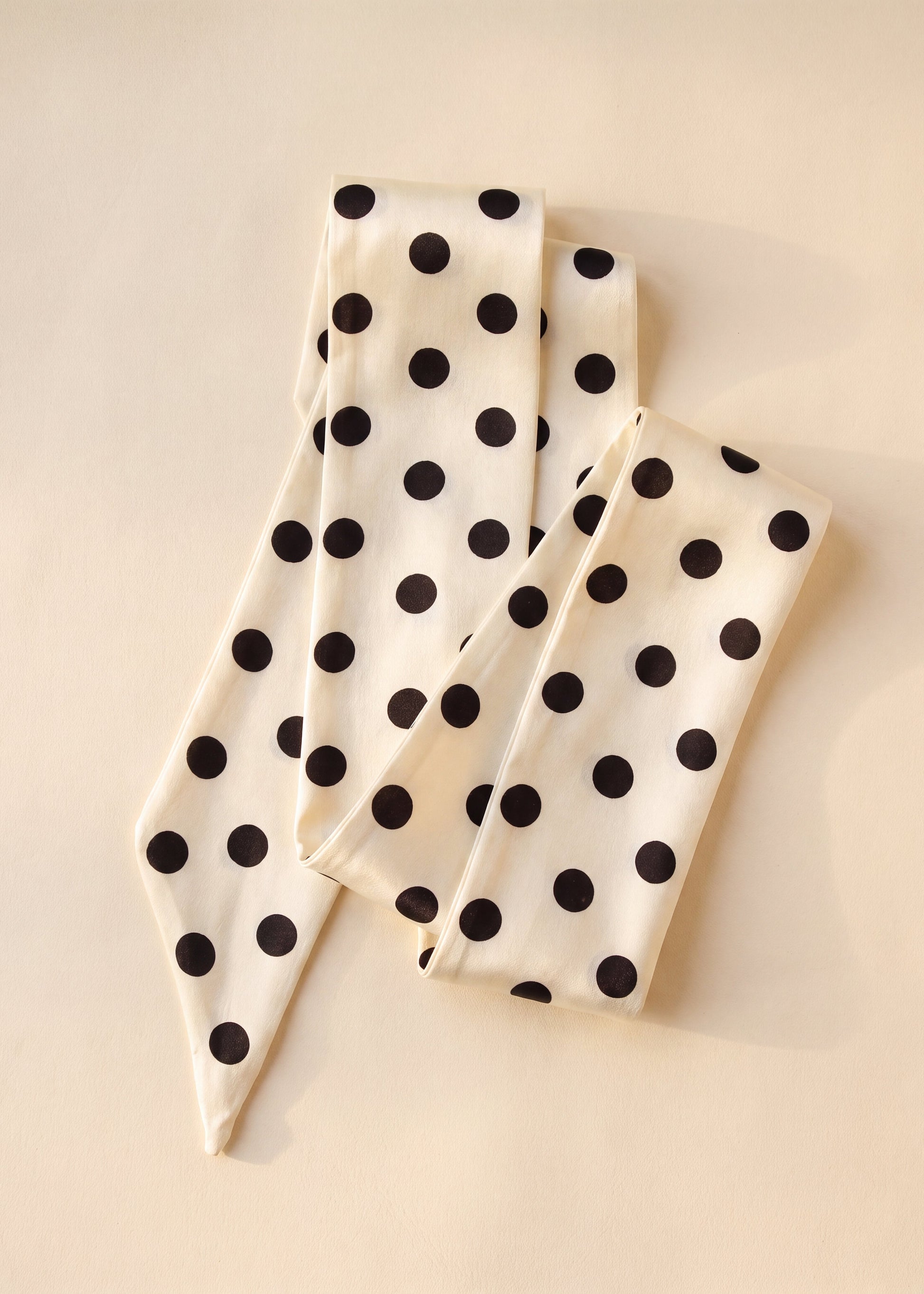 A cream-colored silk scarf with black polka dots, folded neatly on a light beige background.