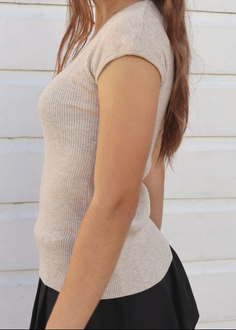 Woman wearing a beige top and black skirt against a white wooden wall