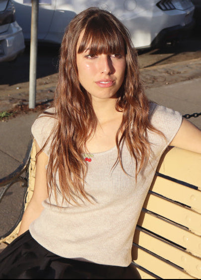 Woman sitting on a bench in a parking lot with cars and a palm tree in the background.