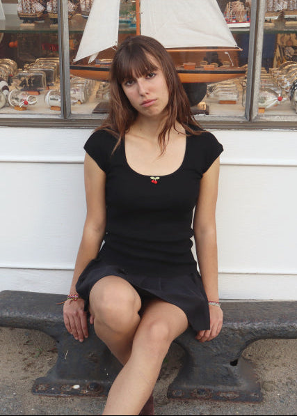 Woman sitting on a bench in front of a white wall with framed pictures.