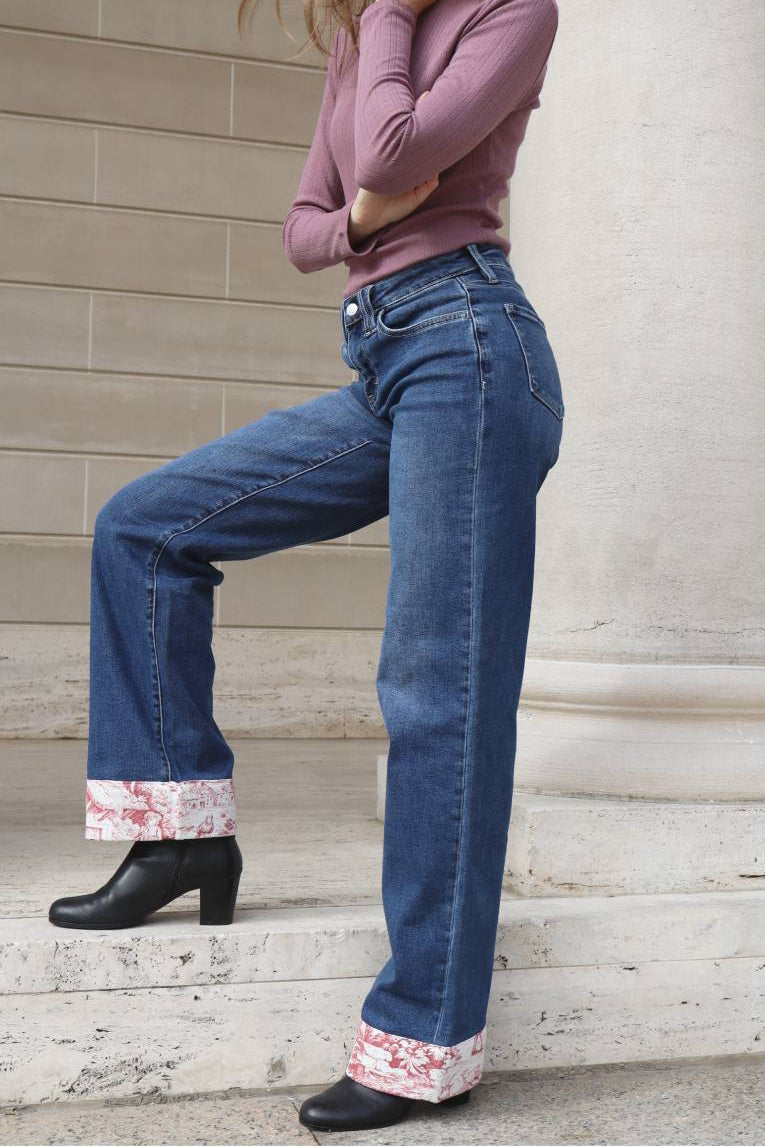 Person wearing blue jeans with floral cuffs standing on steps against a beige wall.