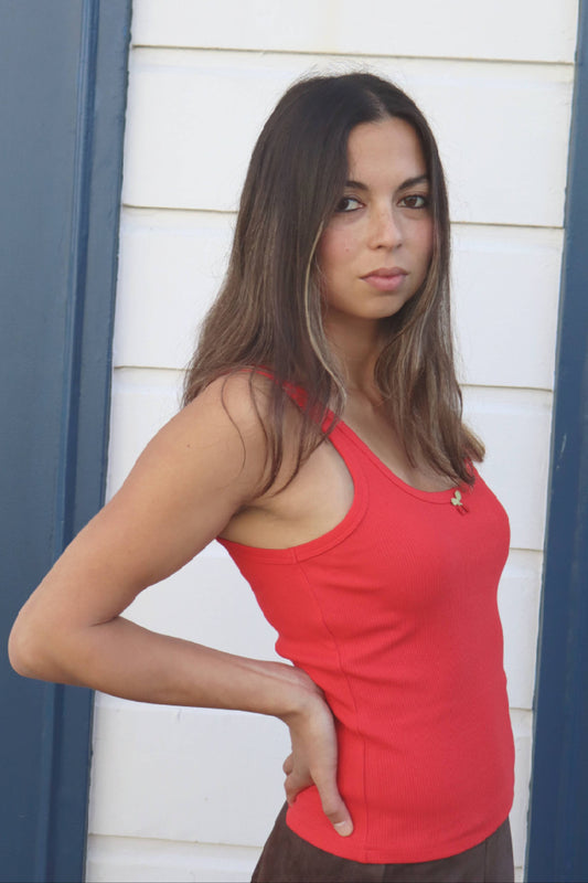 Woman wearing a red tank top standing against a white wall with blue trim.
