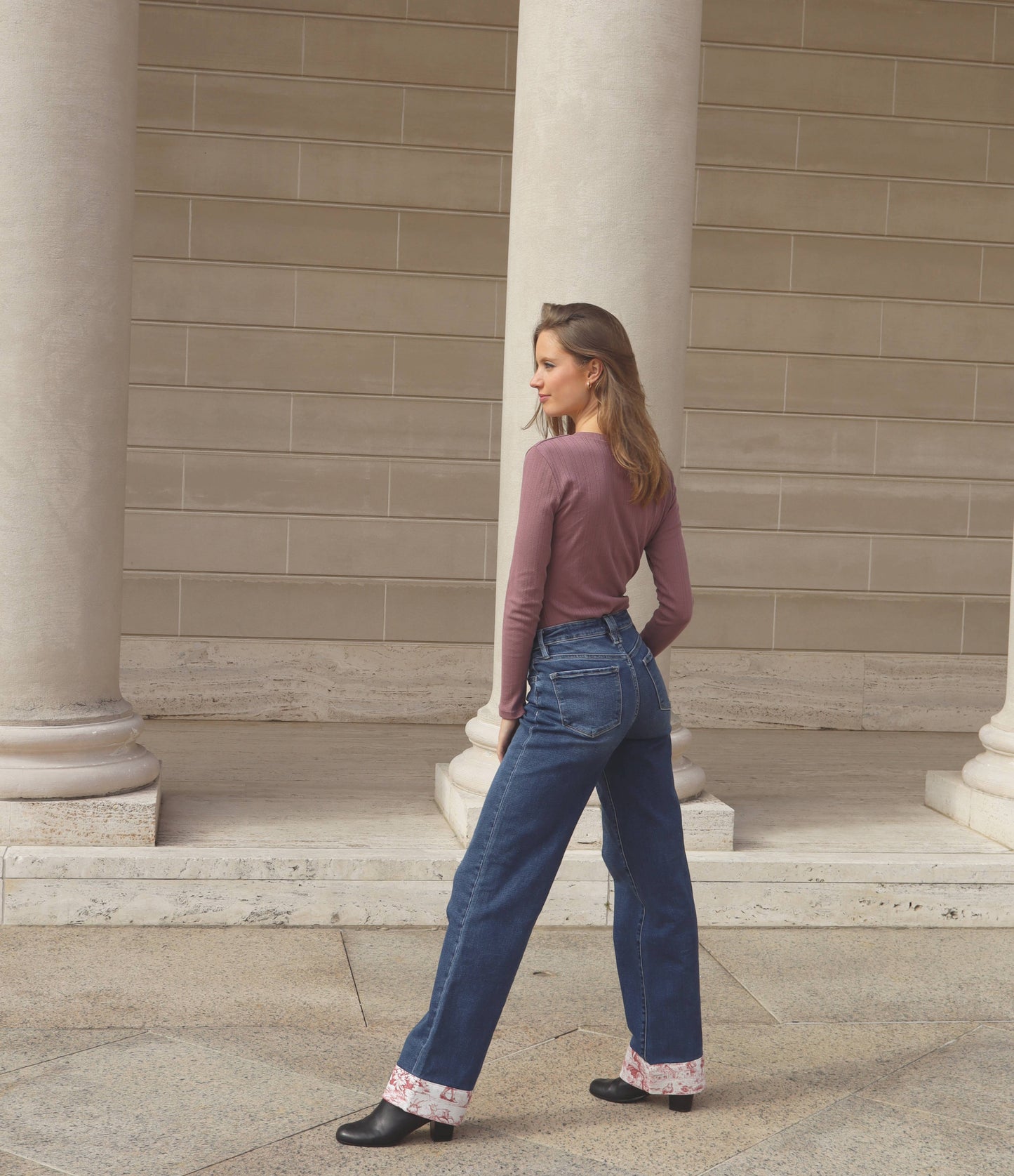 Blonde woman in wide leg blue jeans with red toile de jouy and purple long sleeve top and black boots.