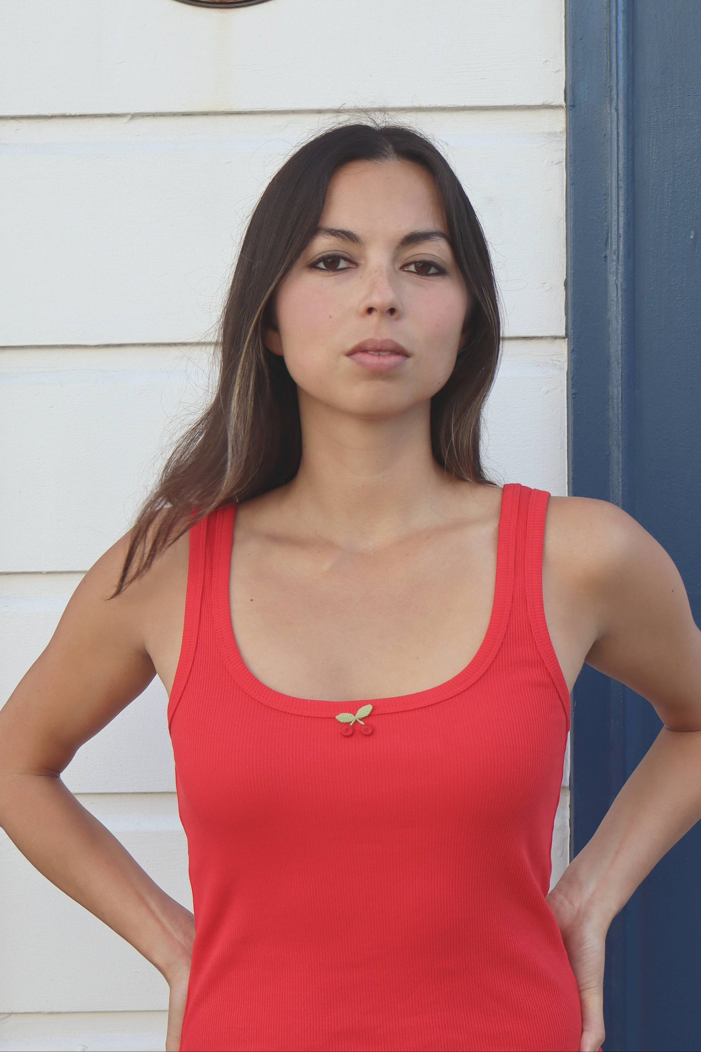 Woman wearing a red tank top standing against a blue door with a white wall background.