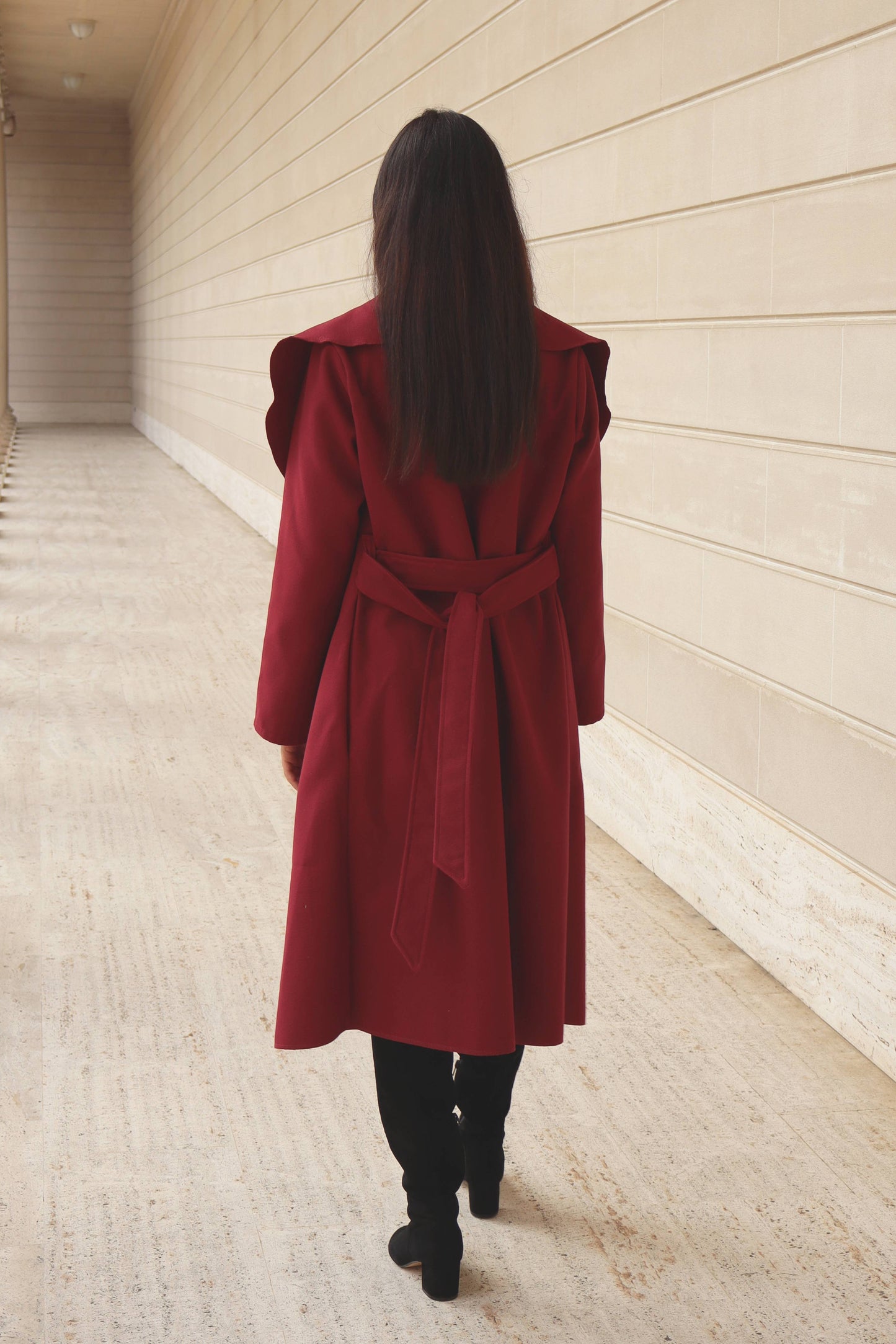 Woman with black straight hair in red coat and suede boots against a marble background at the Legion of Honor in San francisco.