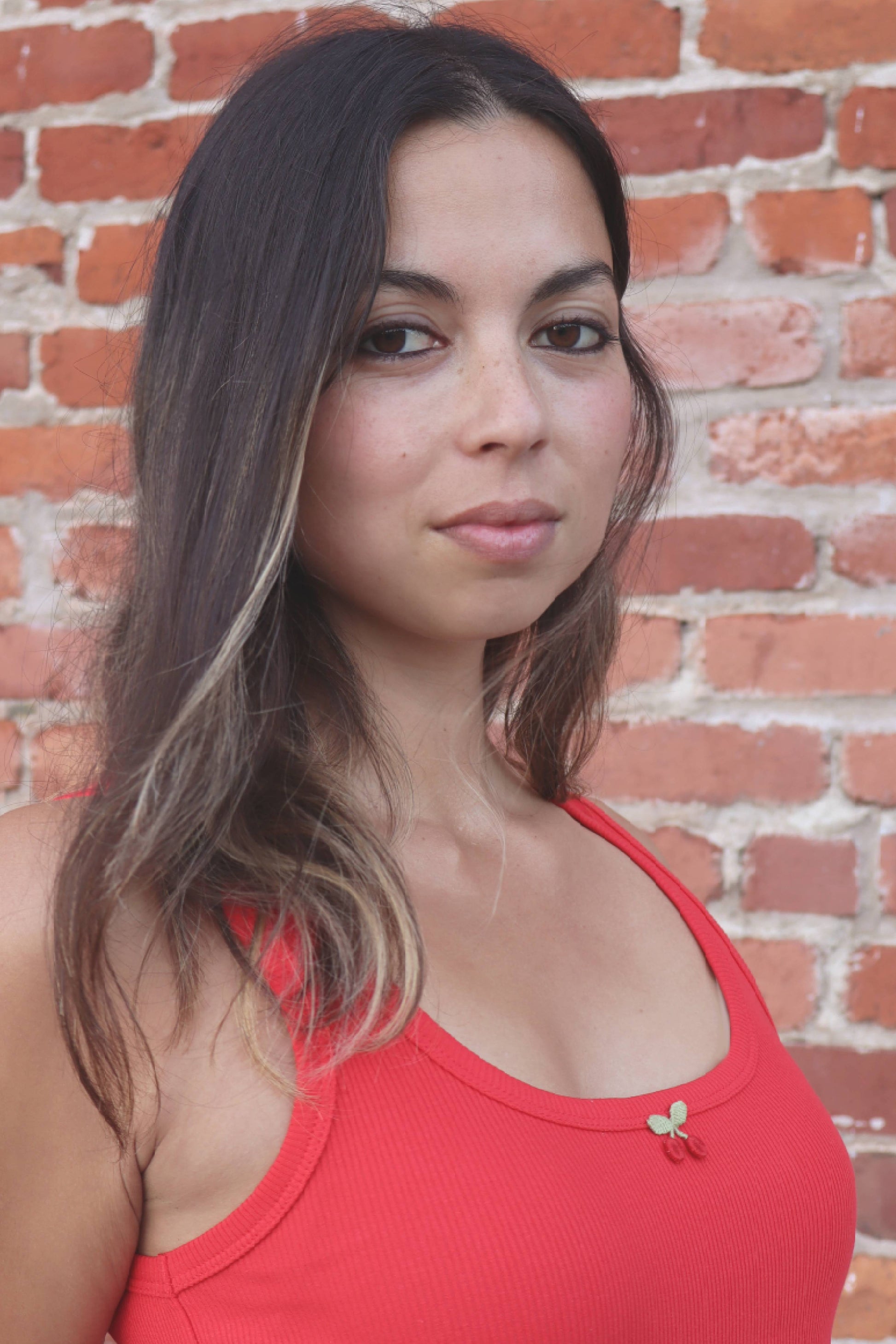 Woman wearing a red tank top against a brick wall