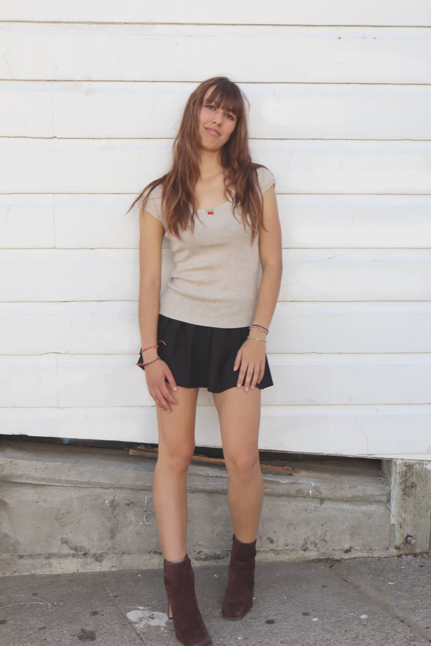 Woman wearing a beige top and black skirt standing against a white wooden wall.