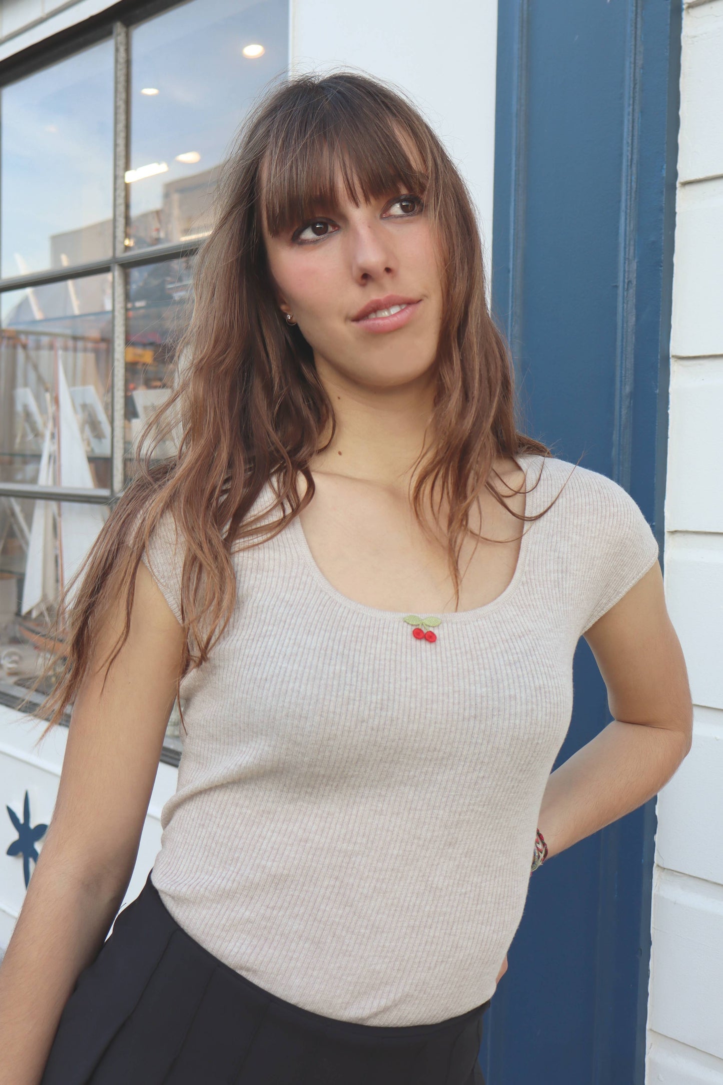 Woman wearing a beige top with a red flower detail, standing in front of a window.