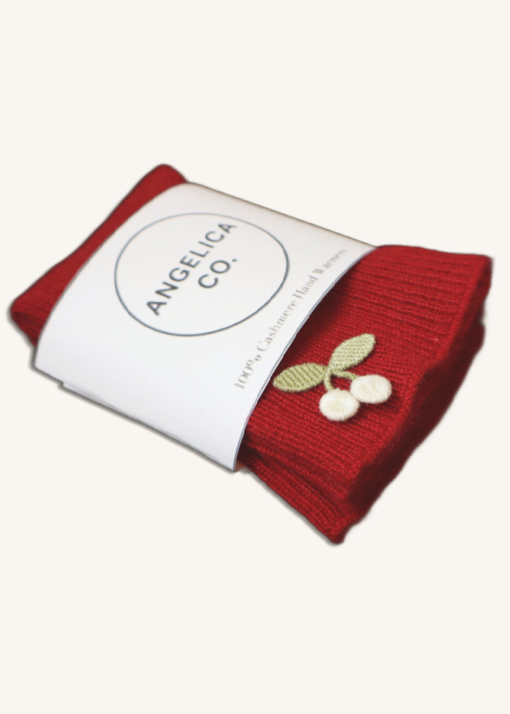 Red knitted item with a cherry design on a white background, featuring the brand 'Angelica Co'.